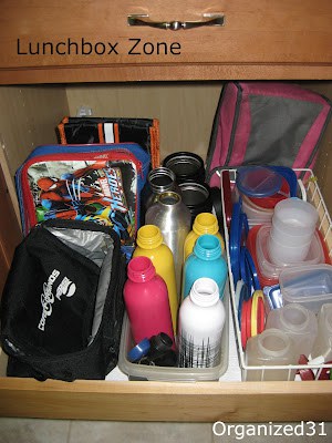 lunch boxes and water bottles organized in bins in a kitchen cabinet