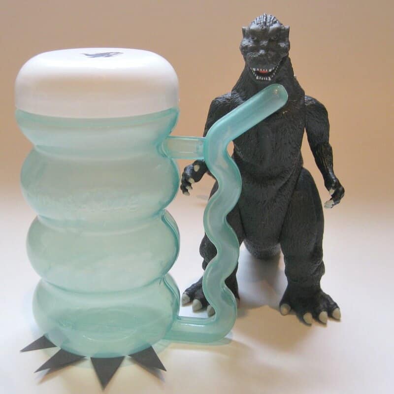 a cup with a plastic Godzilla looking like it's drinking from the straw