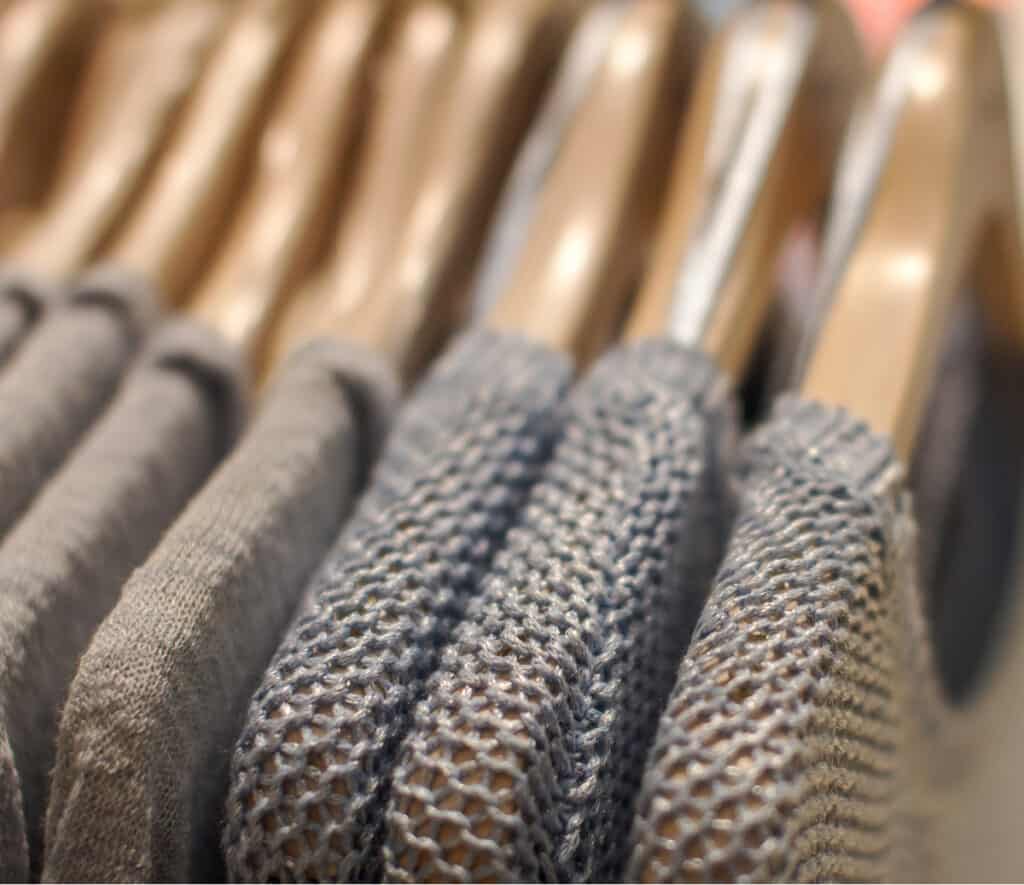 multiple grey sweaters on wood hangers.