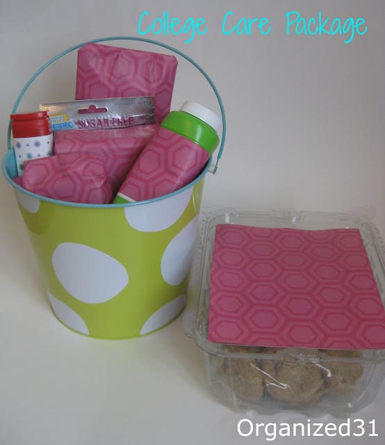 a college care package in a green and white bucket and clear tub with the items wrapped in pink paper