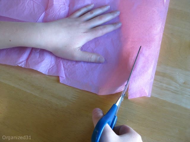 child's hands holding scissors and cutting tissue paper