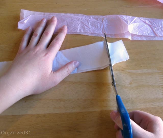 child's hands holding scissors and cutting tissue paper strips