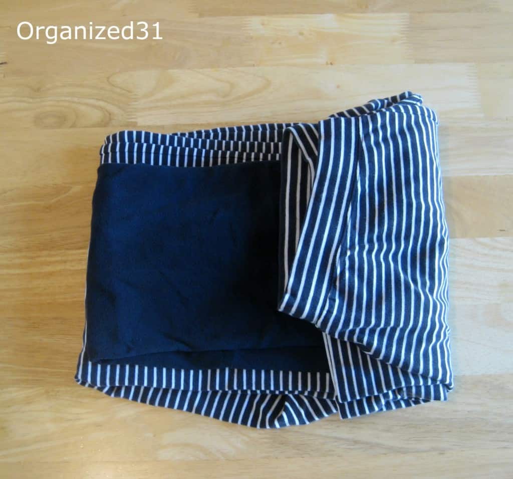 overhead view of neatly folded blue shirt on top of neatly folded navy and white stripe pajama pants with one end folded inward.