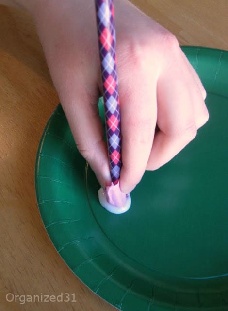 child's hand dipping pencil with tissue paper in glue