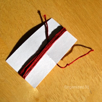 red embroidery floss wrapped around a card on a brown table