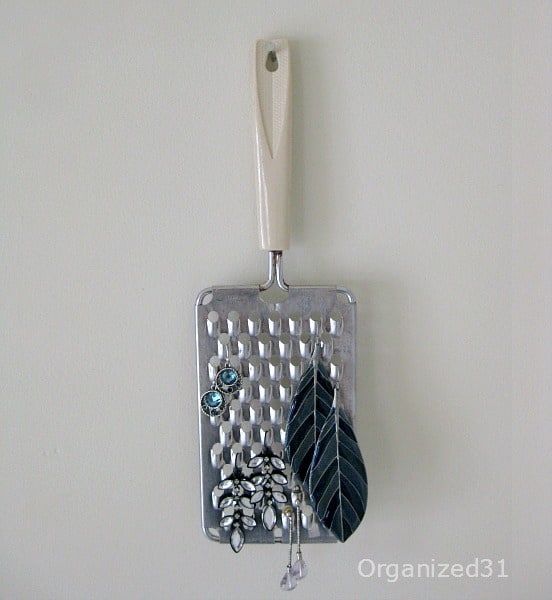 a cheese grater hanging on the wall with earrings hanging from it
