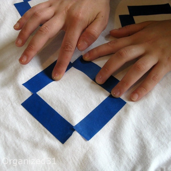 hands putting blue tape on a white t-shirt
