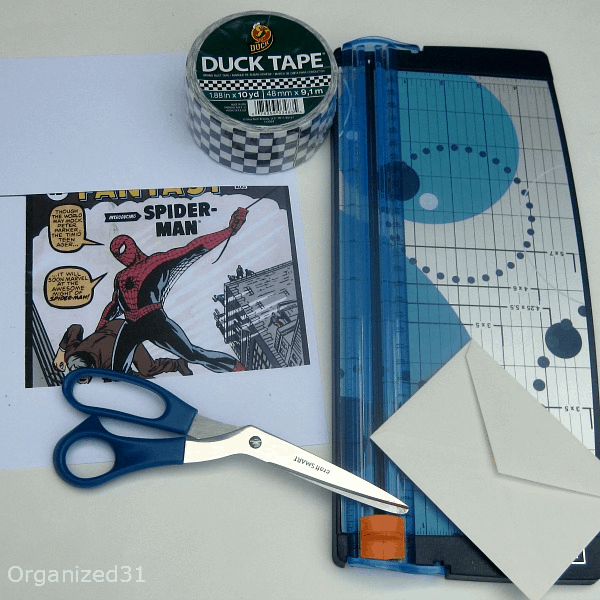 paper cutter, scissors, envelop, checkered Duck tape roll, and photocopy of Spider-man comic book.