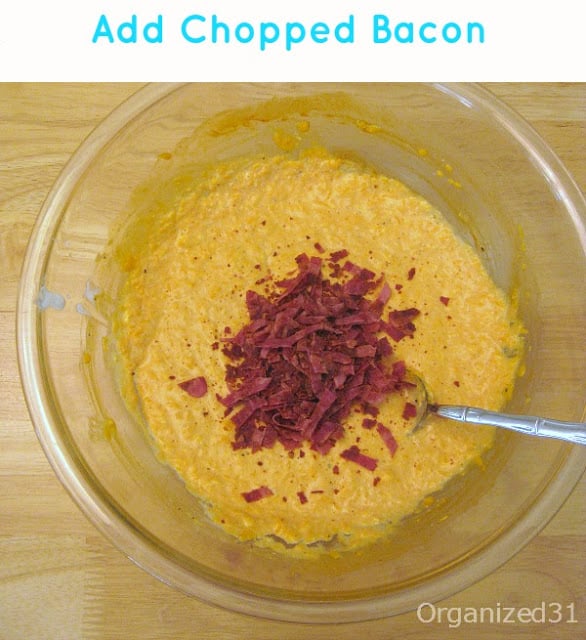 overhead view of glass bowl with orange dip and bacon pieces and metal spoon and title text reading Add Chopped Bacon