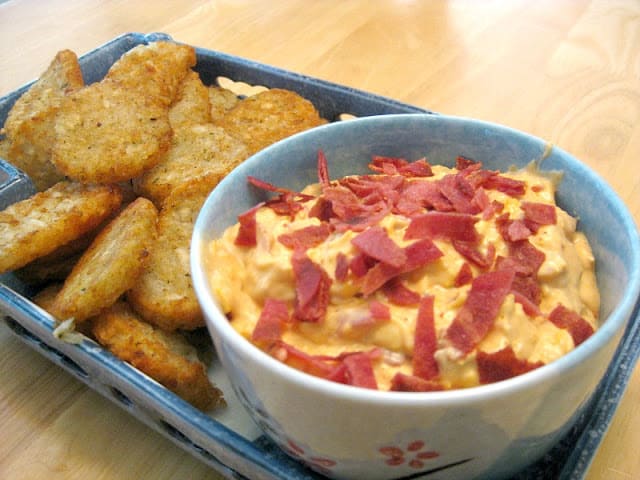 light blue bowl with orange dip with bacon garnish next to potato pieces on blue tray