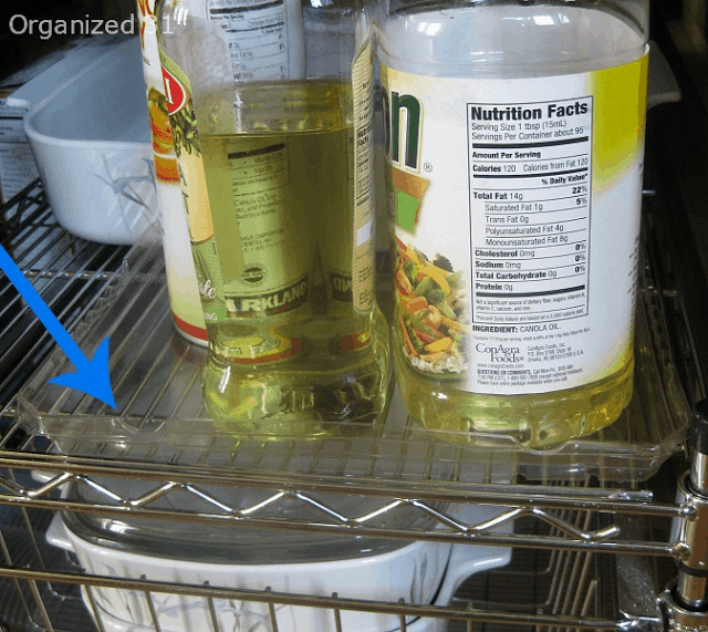 an arrow pointing to a clear tray under bottles of oil on a wire shelf.