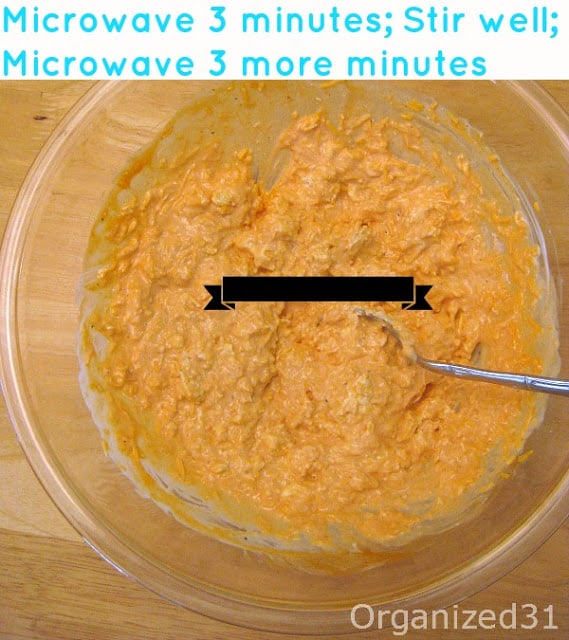 close up of orange dip in large glass bowl with metal spoon with title text reading Microwave 3 minutes; Stir well; Microwave 3 more minutes