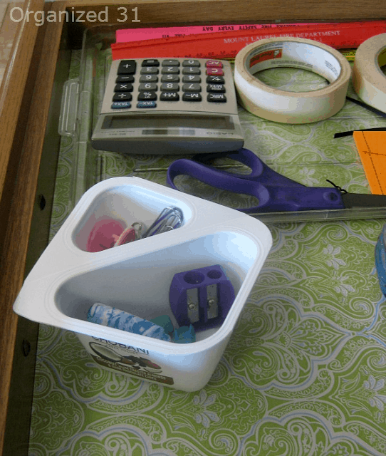 square 2 compartment yogurt cup holding junk drawer items, paper clips and pencil sharpener.