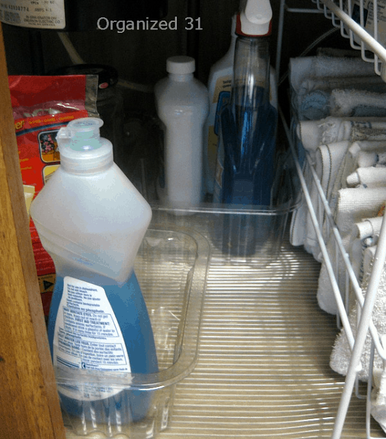 2 clear containers holding bottles of cleaning supplies under kitchen sink