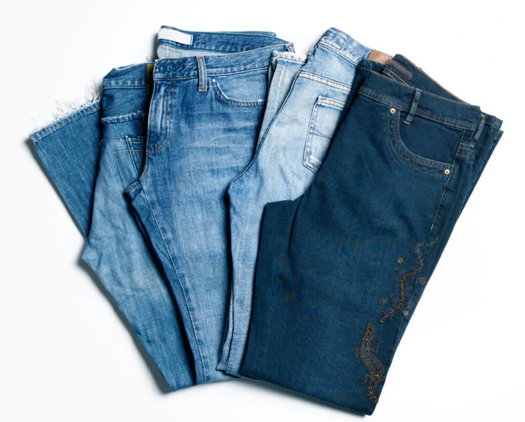 4 pairs of folded jeans in different shades on white background.