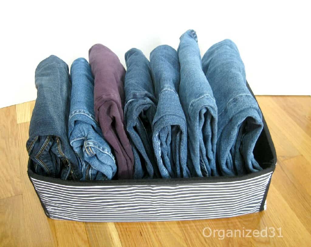 neatly folded jeans organized in a blue striped bin on wood table.
