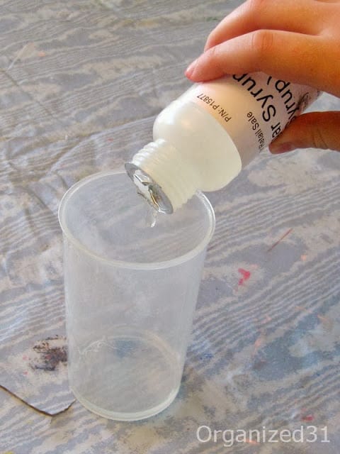 hand pouring bottle of sugar syrup into measuring cup on blue table cloth