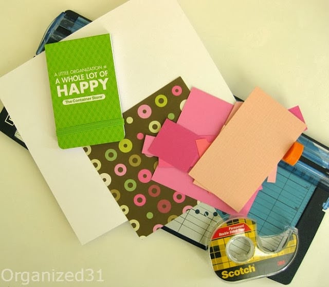 blue paper cutter, stack of colorful paper scraps, double stick tape and small green notebook