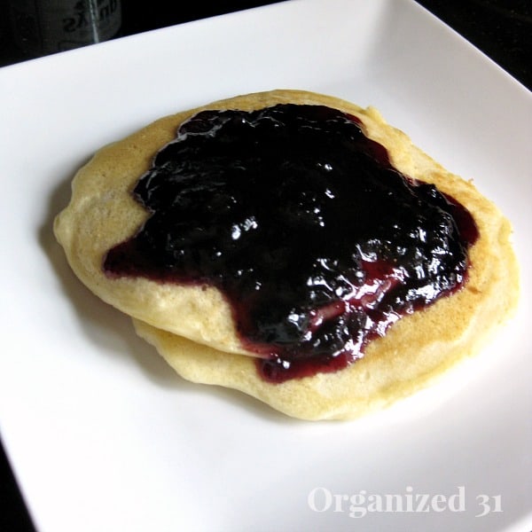 a stack of pancakes topped with Blueberry Syrup on a white plate