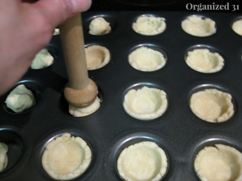 a hand using a wooden tool to press cookie dough up the sides of a muffin pan