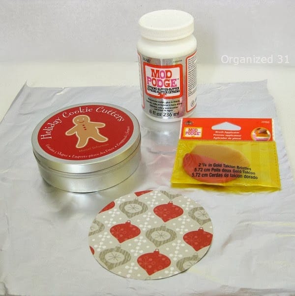 a cookie tin, bottle of mod podge, mod podge brush applicator, decorative paper with ornaments on it
