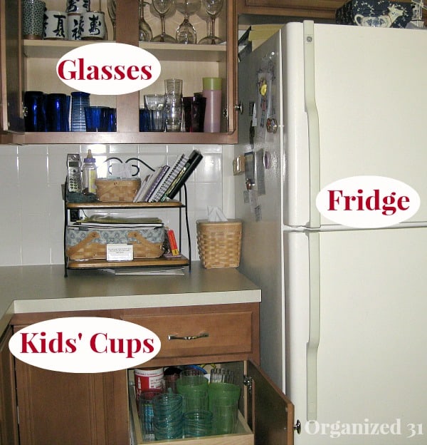 kitchen cabinet with doors open holding glasses, next to tan refrigerator with text overlays identifying items in cabinets