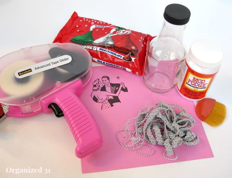 craft supplies, including pink paper, tape, Mod Podge glue, empty bottle and bag of candy