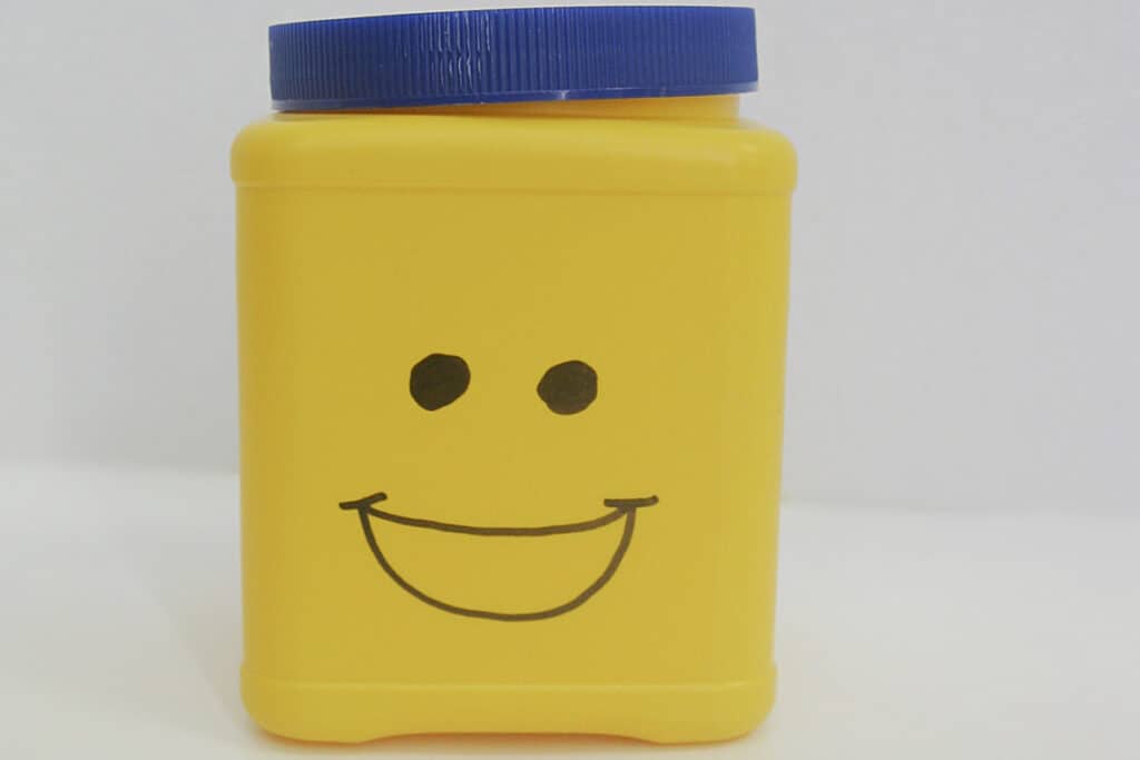yellow can with blue lid and drawn black smiling face.