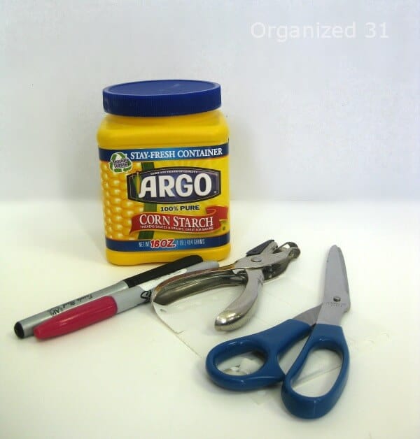 yellow cornstarch can, red and black marker, scissors, hole punch and sheet of white labels on table