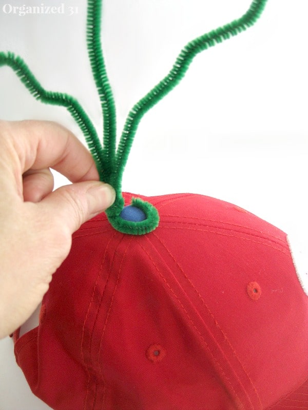 hand holding bent pipe cleaners to top of red hat