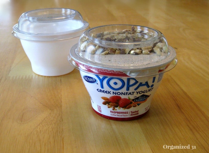 small yogurt cup with clear lid in front and empty white yogurt cup in back on wood table