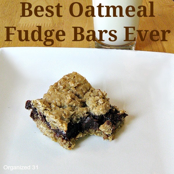 an oatmeal fudge bar with a bite taken out of it on a white plate next to a glass of milk on a brown table with title text at the bottom reading Best Oatmeal Fudge Bars Ever