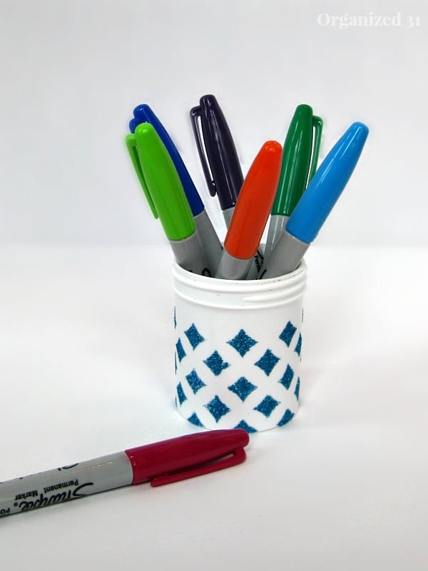 markers in a white container decorated with blue diamonds next to a red sharpie on a white table
