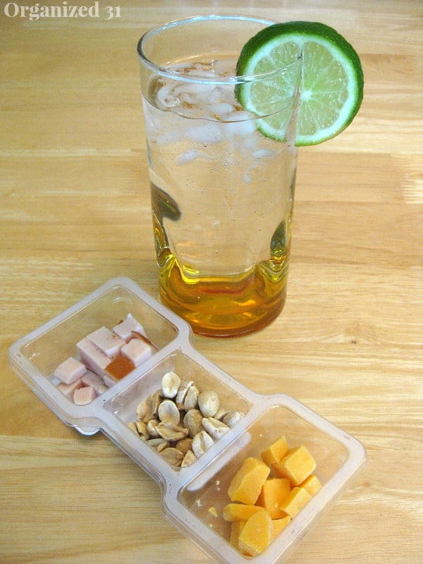 a glass of water with a slice of lime next to a P3 portable protein snack on a brown table