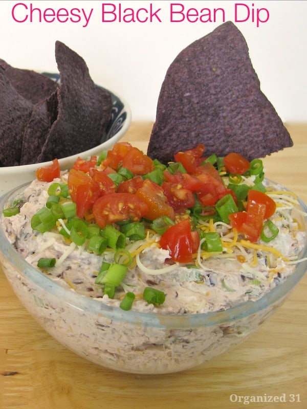 black tortilla chip in bowl of dip with tomato garnish on wood table