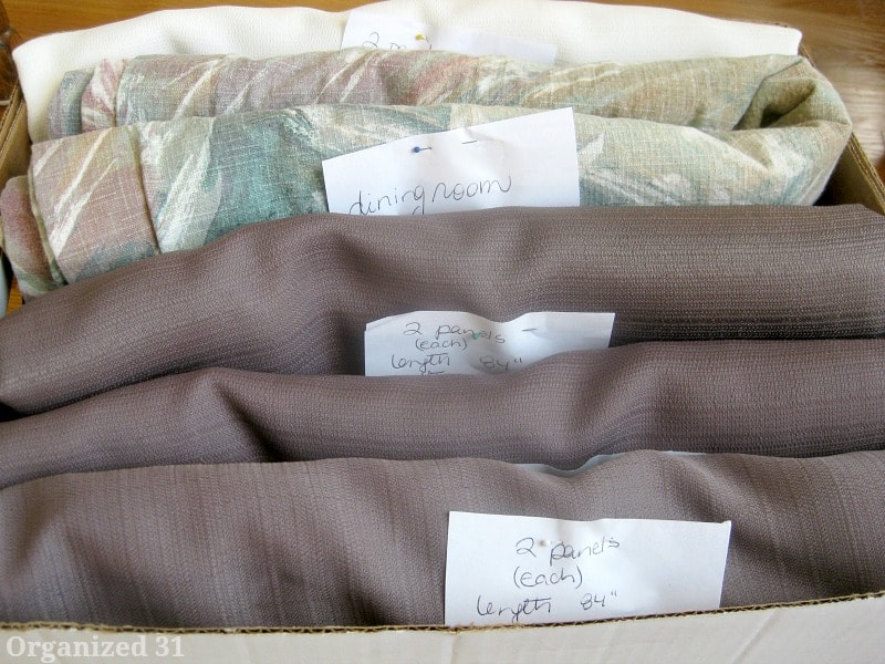 box of neatly folded curtains with dimensions on notes pinned to them