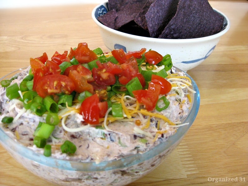 bowl of tan dip with chopped tomatoes in front of bowl of tortilla chips.