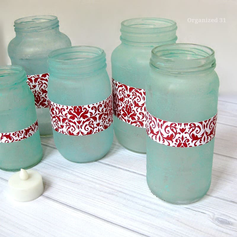 5 light green jars with red and white label on white wood table and small battery candle 