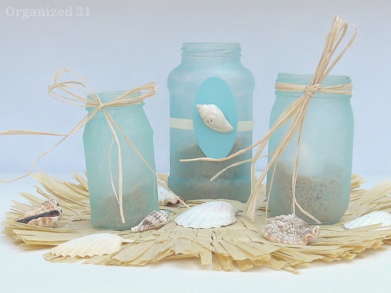 3 light blue jars with raffia bows and shells on raffia mat and shells