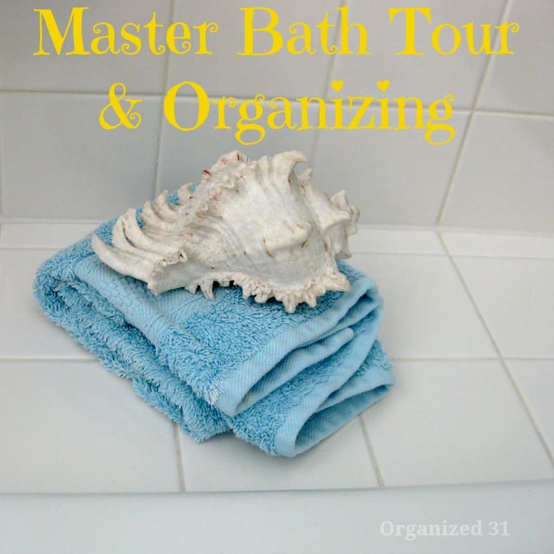 white shell on folded blue towel on white tile counter with title text reading Master Bath Tour & Organizing