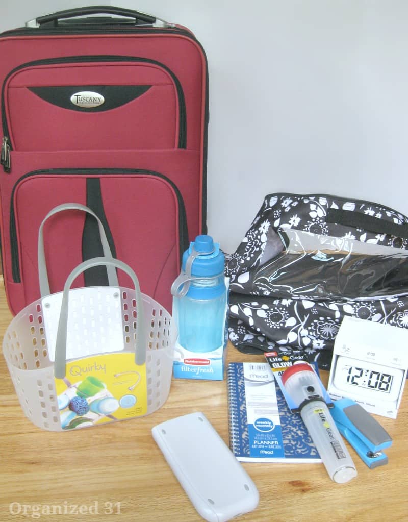 red suitcase, plastic tote, blue water bottle, clock, stapler, flashlight, notebook and calculator on wood table