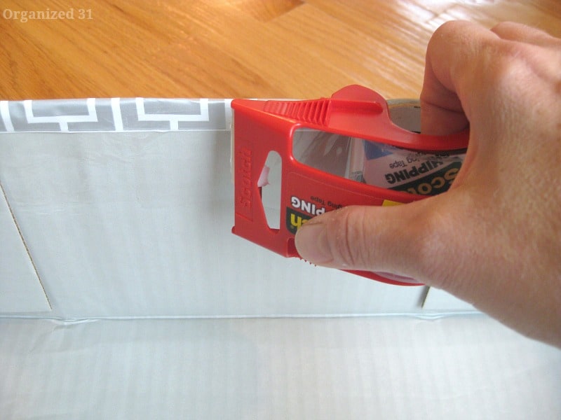 hand holding roll of clear packing tape by edge of paper on box