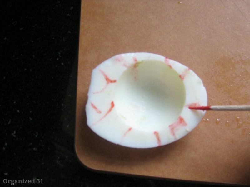 half of hard boiled egg with toothpick drawing red streaks on the edges.