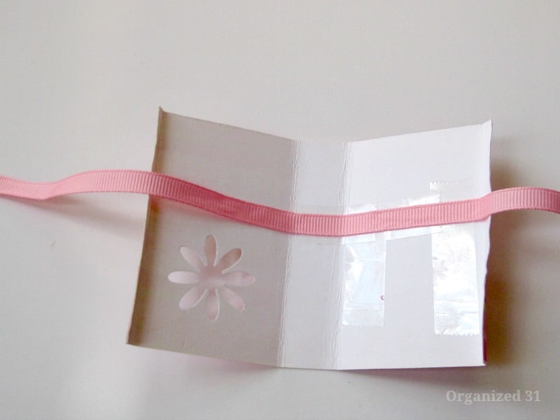 rectangle of folded paper with flower punched out of one side and pink ribbon attached