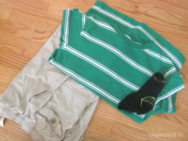 folded tan shorts, with folded green and white striped t-shirt and pair of black socks on top
