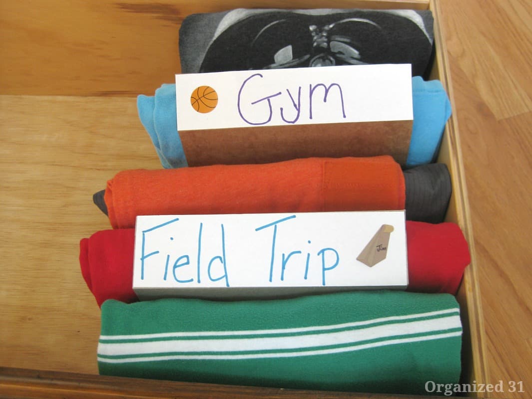 overhead view of clothes folded neatly in drawer with labels "Field Trip" and Gym