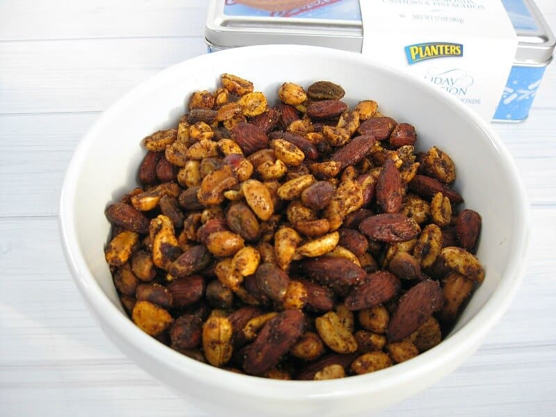 white bowl full of spiced nuts on white wood table.