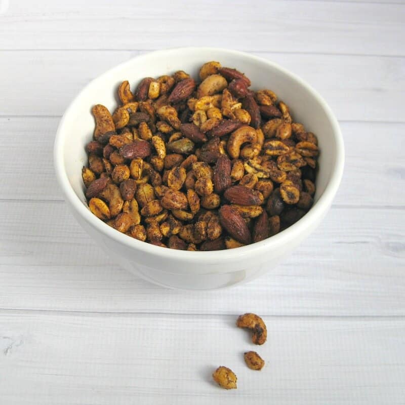 white bowl of spiced nuts on white wood table