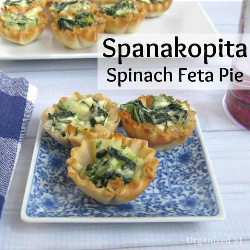 blue and white plate with 3 small spinach tarts on white wood table