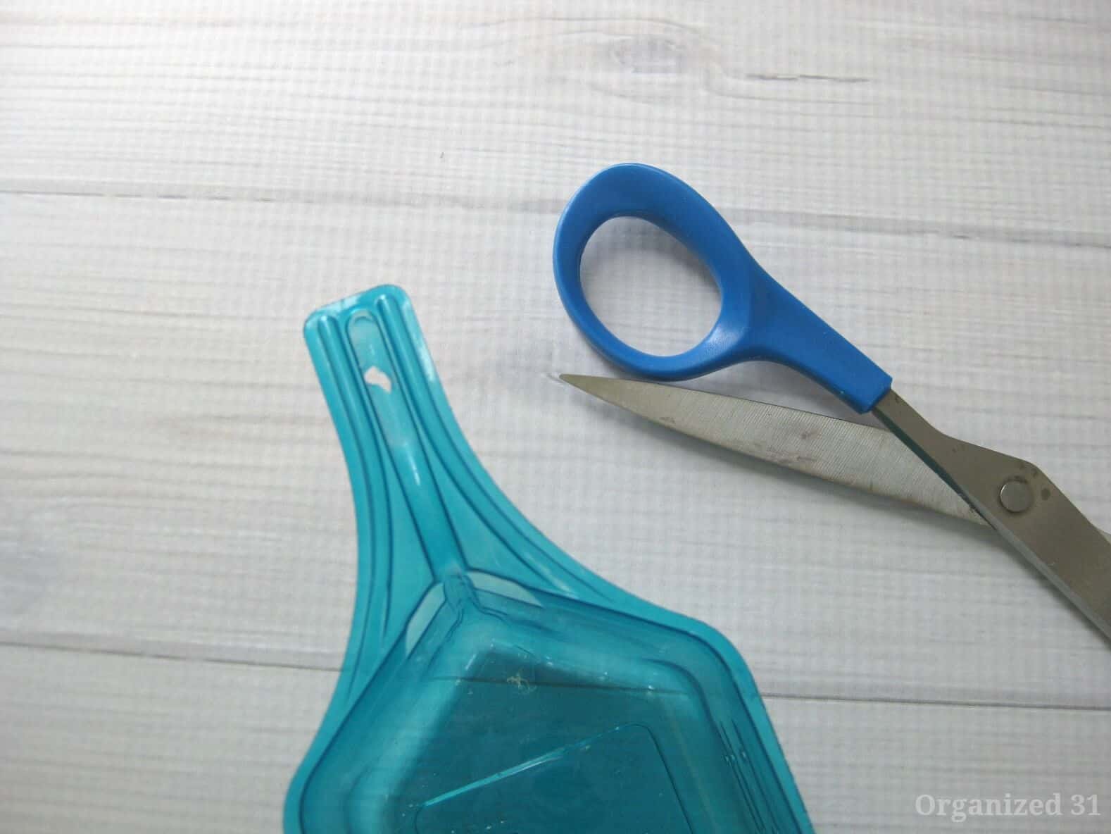 close up of handle of blue plastic laundry scoop and scissors